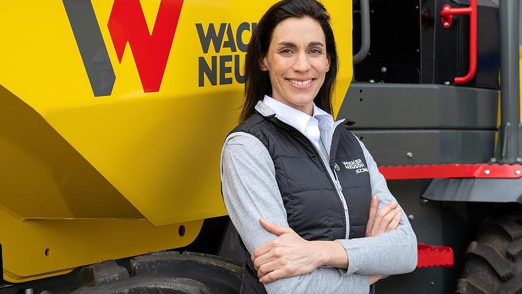 Een medewerker van Wacker Neuson staat glimlachend met gekruiste armen voor een Wacker Neuson-wieldumper.