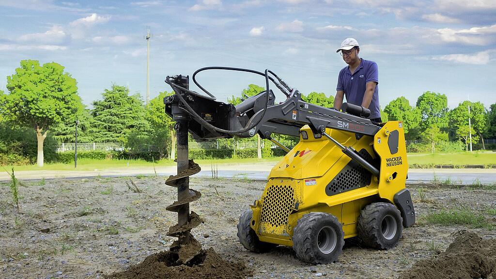 Minilader op wielen met grondboor in actie