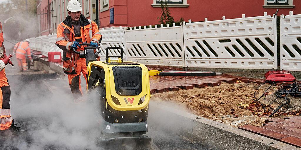 bouwvakker die met een trilplaat werkt op een bouwplaats in de binnenstad