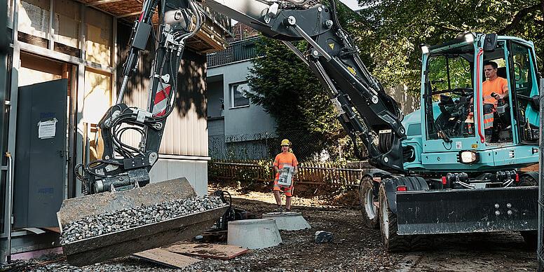 Wacker Neuson EW100 wheeled excavator handling bulk material with a tilt bucket attachment on a construction site.