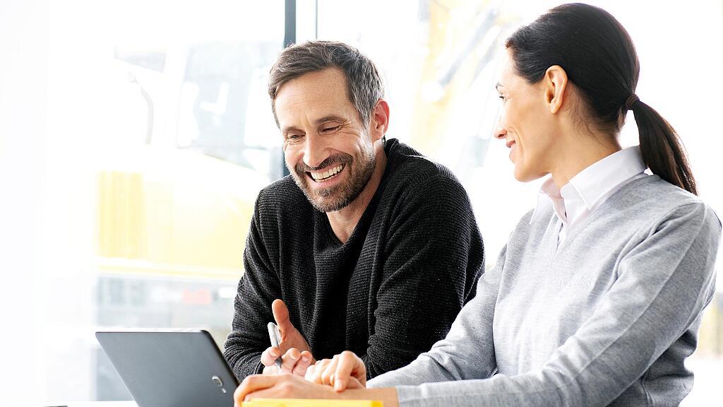 Klant zit achter een laptop met een verkoopster van Wacker Neuson en krijgt advies over tweedehands bouwmachines en bouwmateriaal.