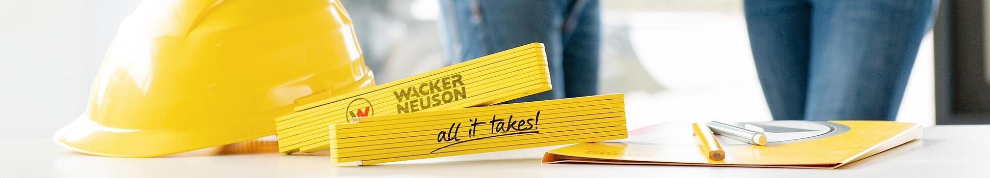 Wacker Neuson merchandise items lying on table in foreground, Wacker Neuson employees in background.