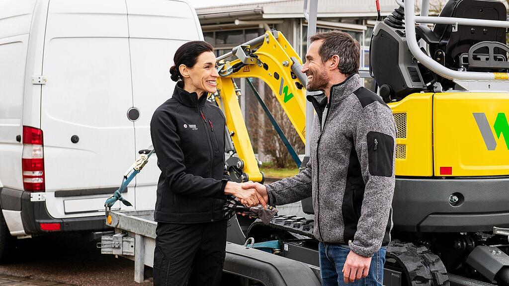 Een medewerker van Wacker Neuson schudt de hand van een klant voor een Zero Emission-rupsgraafmachine van Wacker Neuson.