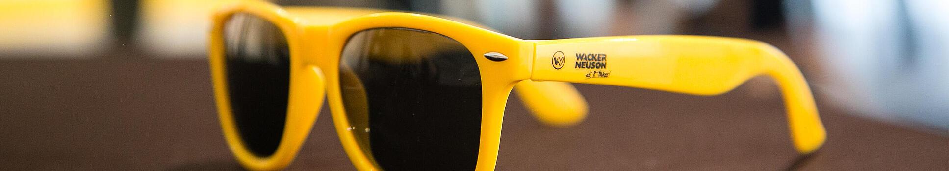 Yellow sunglasses with Wacker Neuson logo.