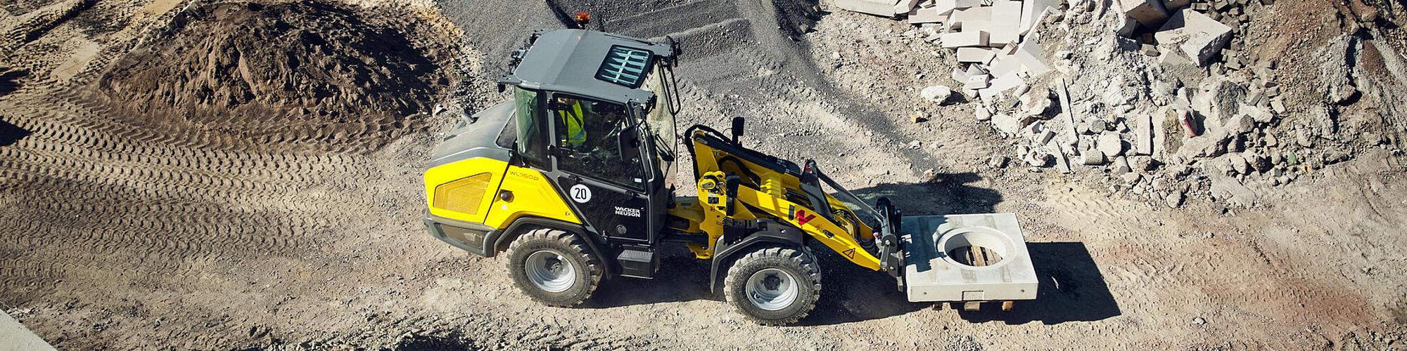 Een Wacker Neuson WL750p-wiellader die een betonelement vervoert op een bouwplaats.