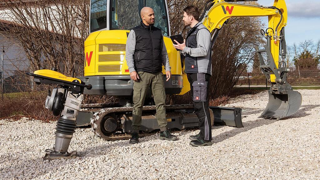 Wacker Neuson employee advising customer about the WeCare package in front of Wacker Neuson machines.